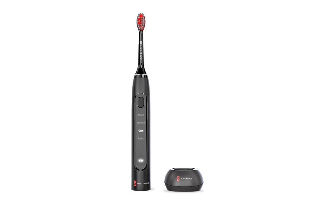 Black electric toothbrush with red bristles next to toothbrush holder